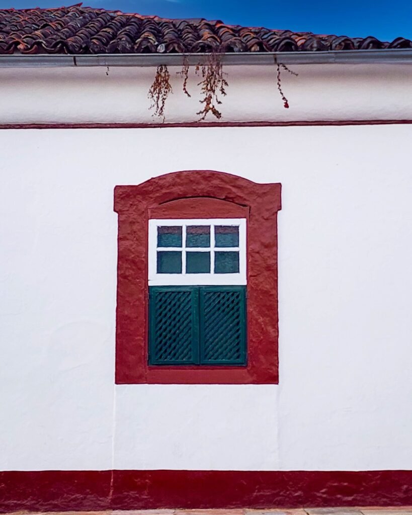 Janela colonial com moldura vermelha e veneziana verde em fachada branca
