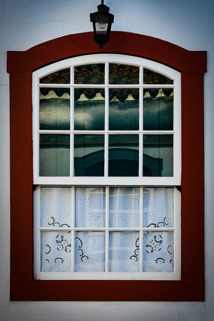 Janela colonial com moldura vermelha e veneziana verde em fachada branca