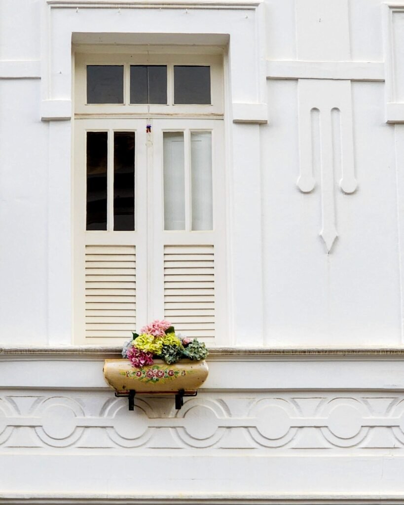 Janela colonial com moldura vermelha e veneziana verde em fachada branca