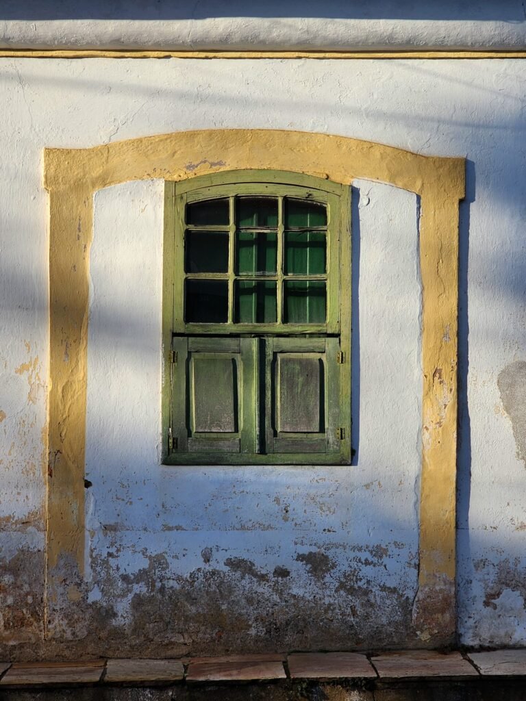 Janela colonial com moldura vermelha e veneziana verde em fachada branca